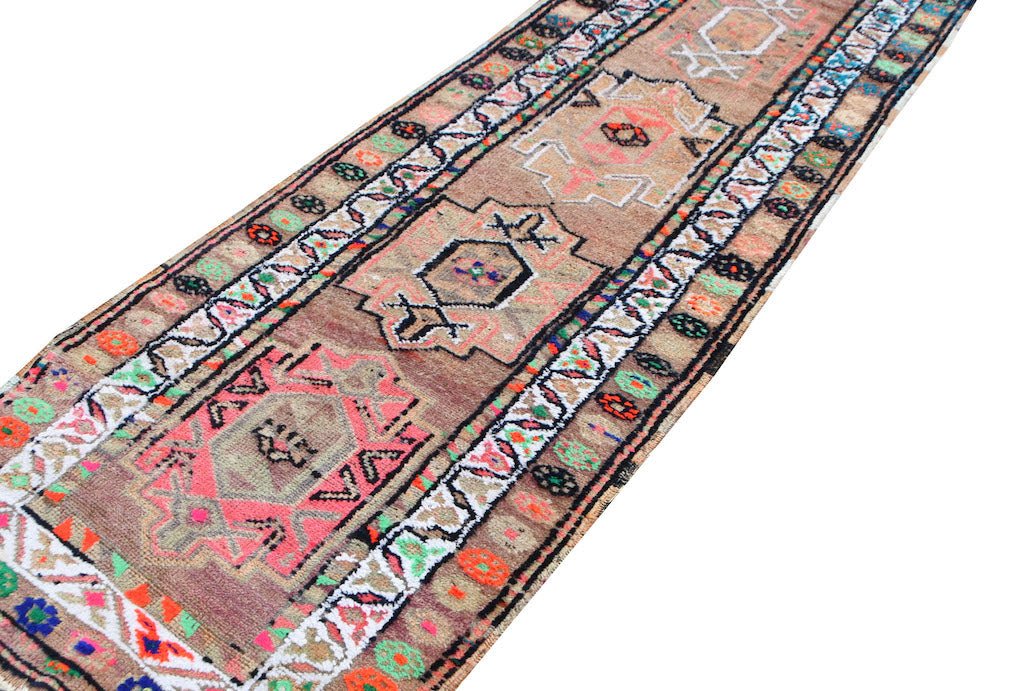 A vintage Kurdish Herki runner featuring tribal motifs in neon colors on a wool base.