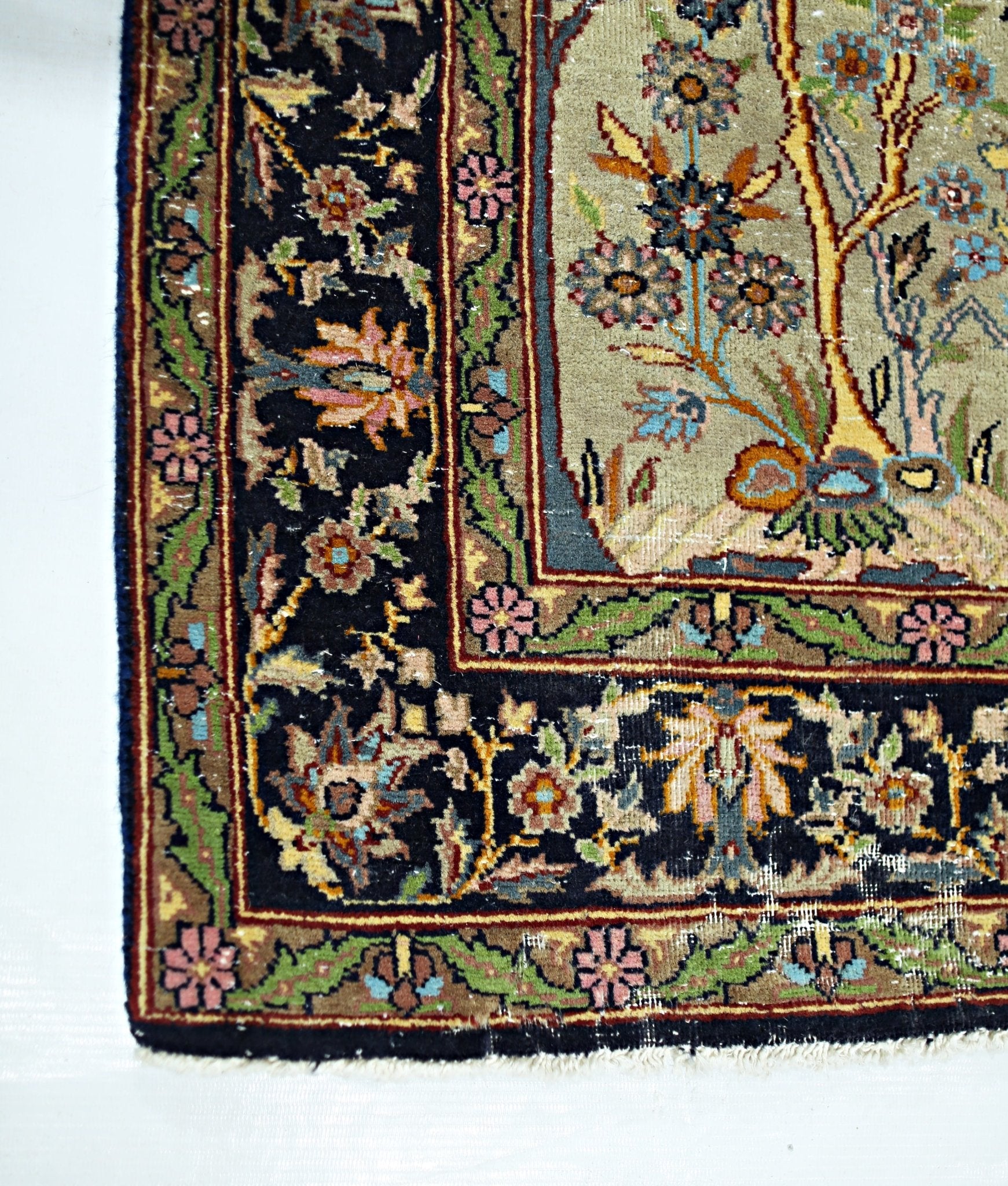 A corner detail of a vintage Persian prayer rug featuring intricate floral patterns on a black border.