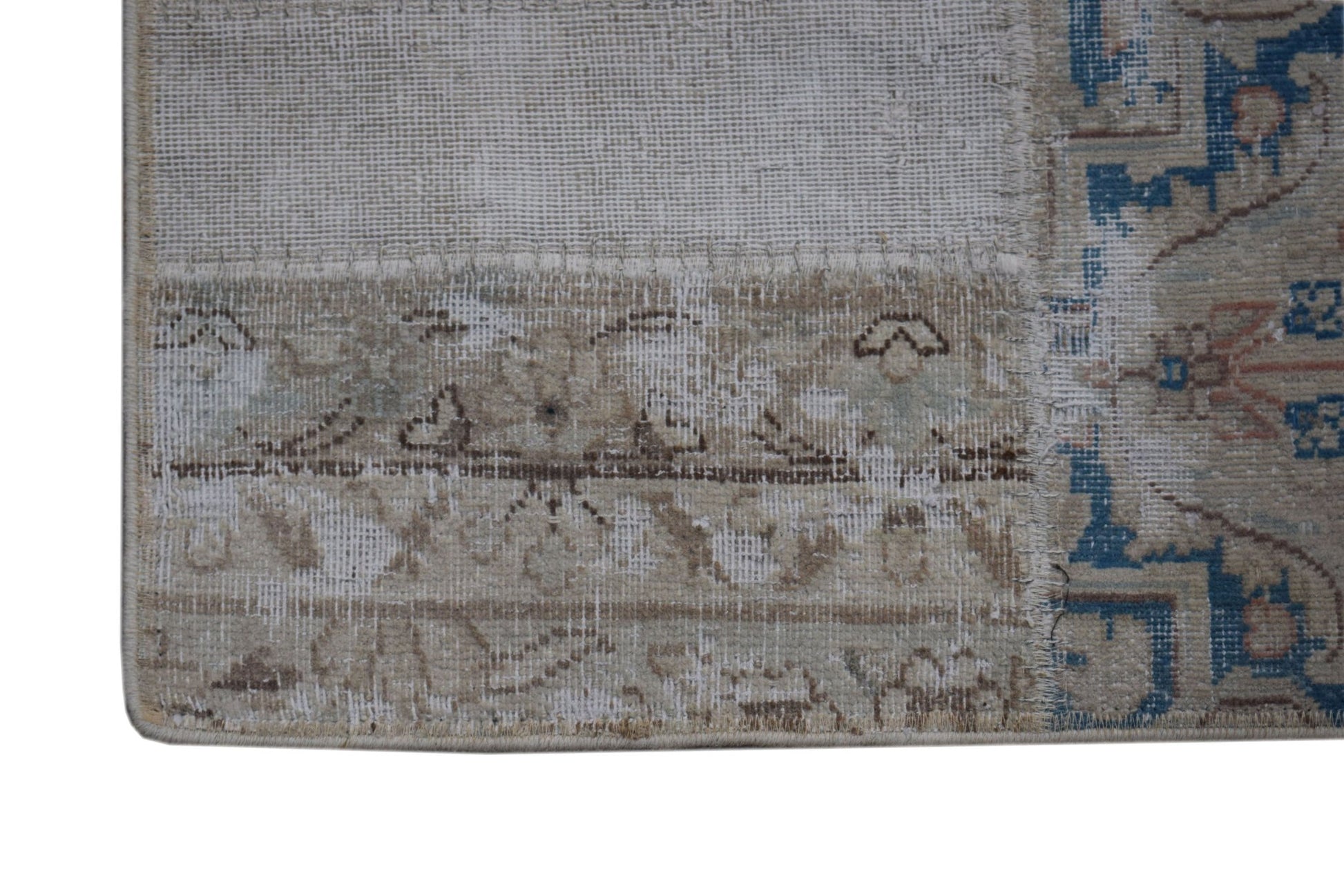 A close-up of a handmade vintage patchwork rug featuring faded blue and beige floral patterns.