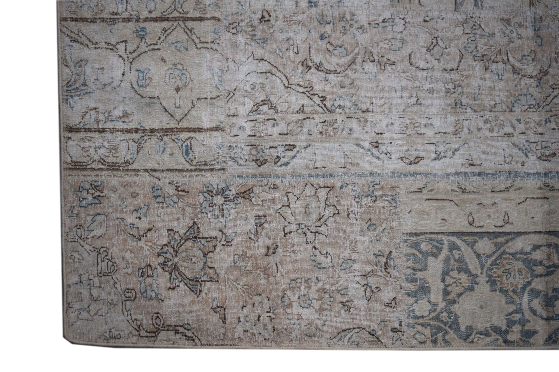 A handmade vintage patchwork rug featuring a faded floral pattern in shades of beige and blue.