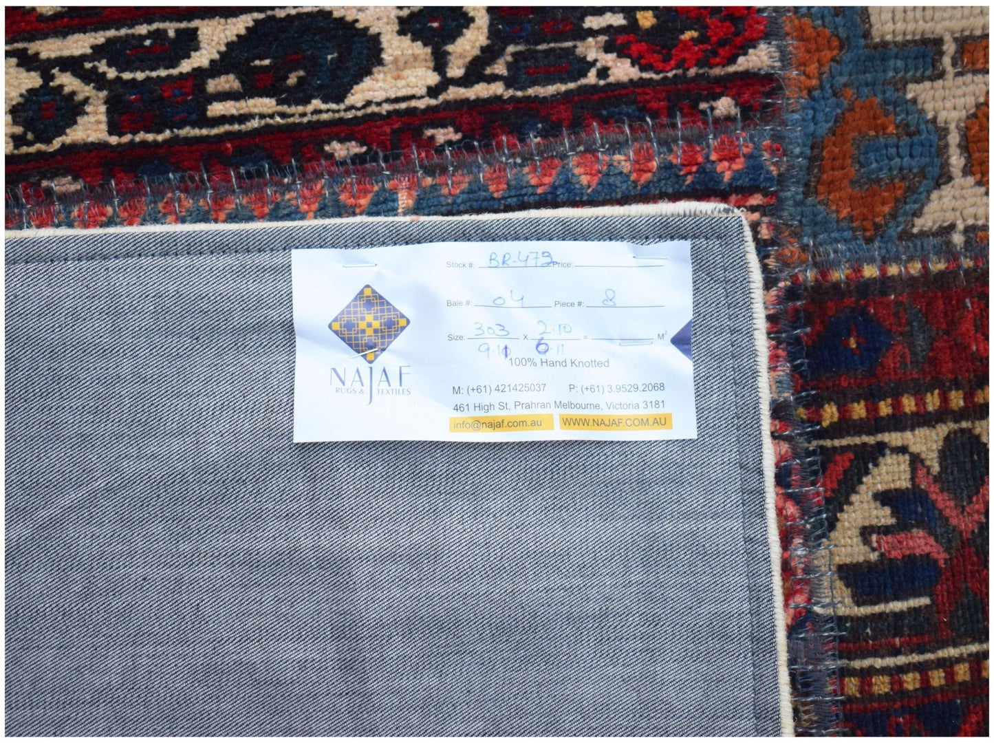 The underside of a vintage patchwork rug showing a product label on a grey fabric backing.