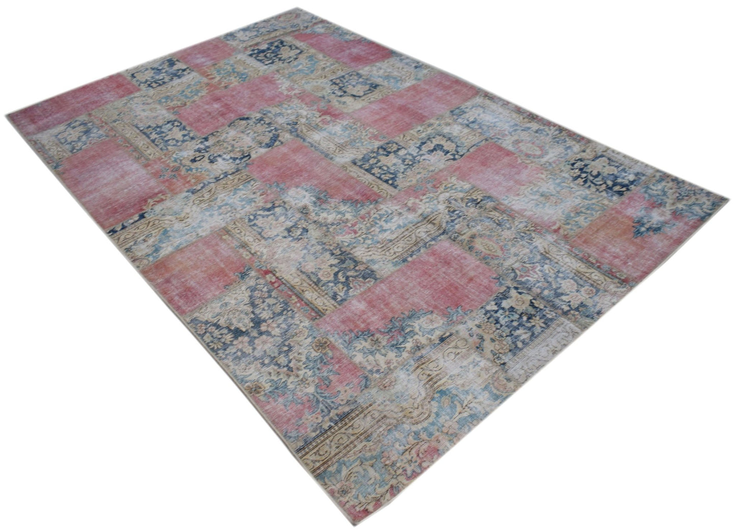 A rectangular vintage patchwork rug featuring a faded floral pattern in shades of pink and blue.