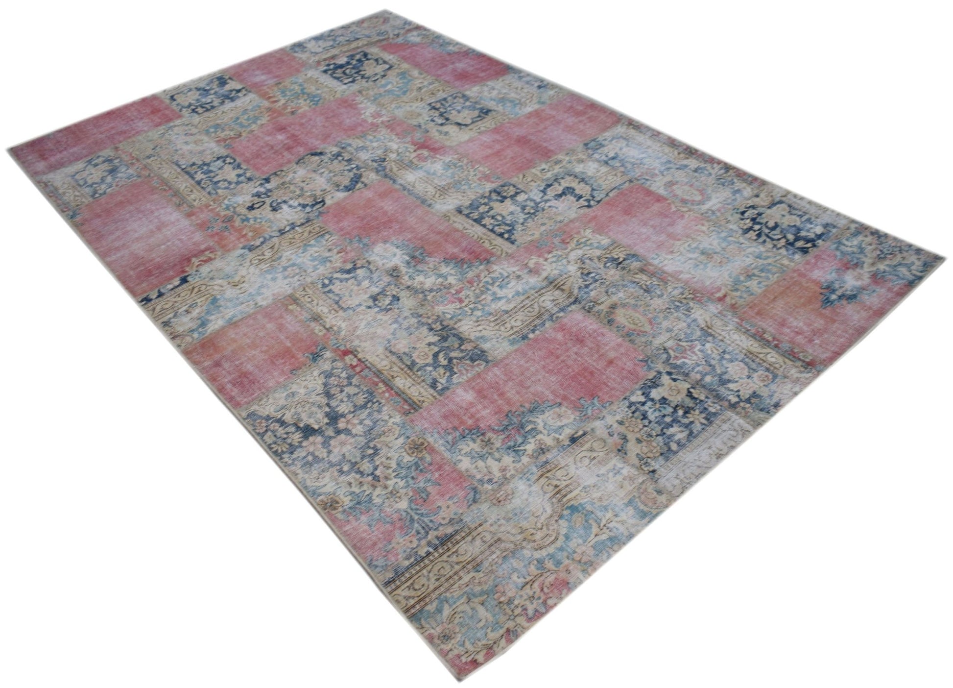 A rectangular vintage patchwork rug featuring a faded floral pattern in shades of pink and blue.