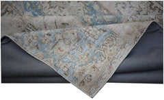 A vintage patchwork rug with a faded blue and beige floral pattern folded over a grey backing.