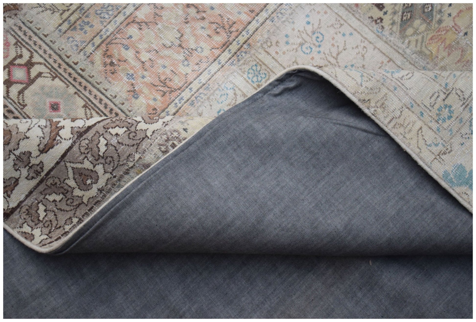 A vintage patchwork rug with a grey fabric backing and intricate floral patterns in muted tones.