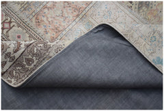 A vintage patchwork rug with a grey fabric backing and intricate floral patterns in muted tones.