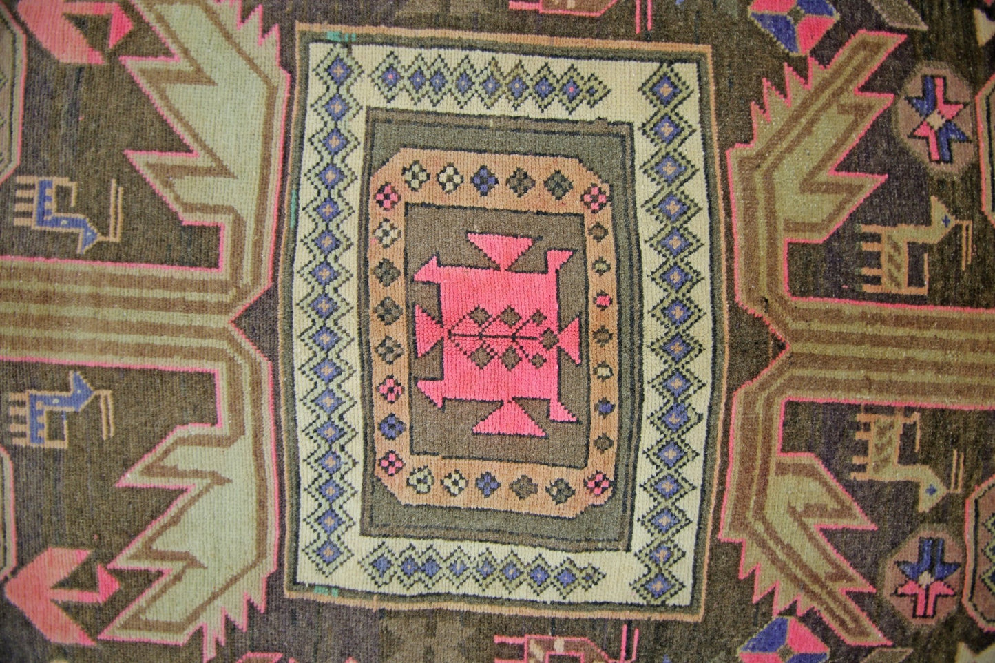 A vintage Persian Ardabil rug featuring a central pink geometric medallion on a dark brown field.