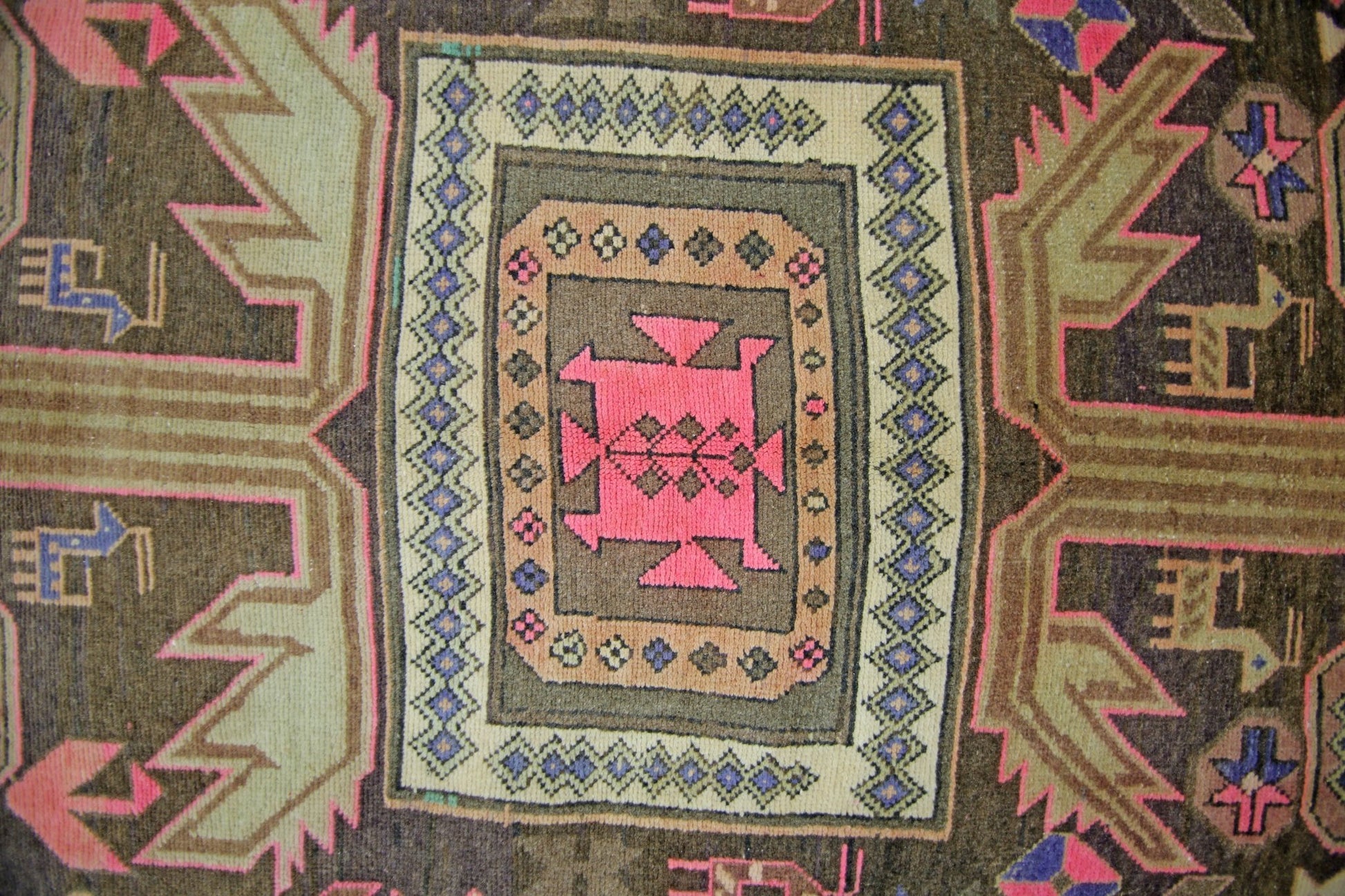 A vintage Persian Ardabil rug featuring a central pink geometric medallion on a dark brown field.