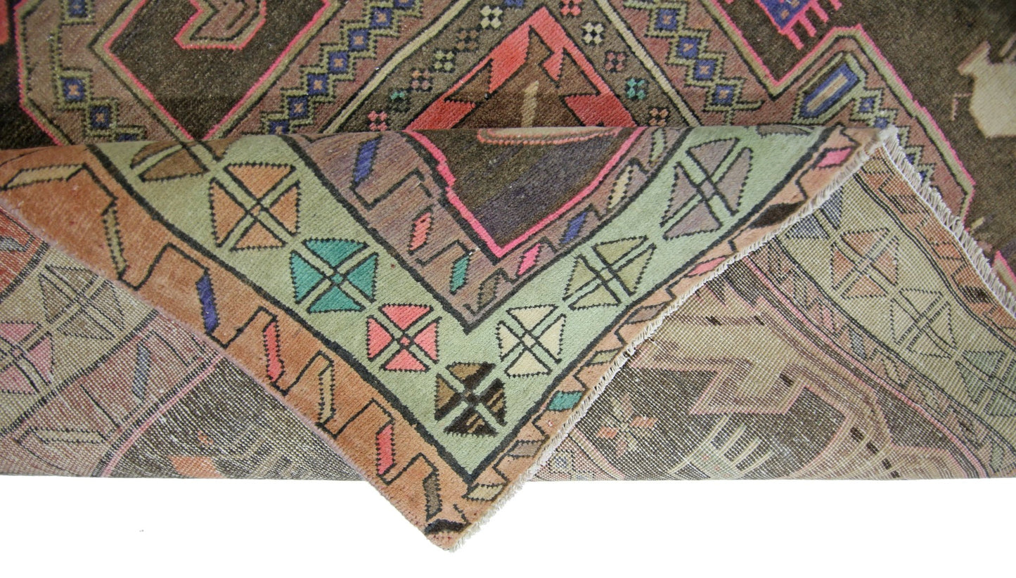 A vintage Persian Ardabil rug featuring geometric patterns in muted tones with a folded corner.