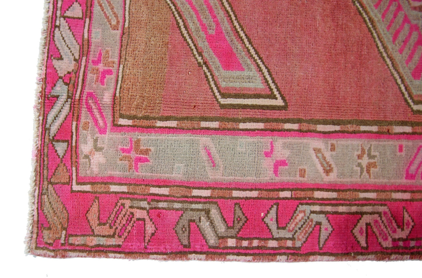 A close-up of a vintage Persian Ardabil rug featuring geometric patterns in pink and grey tones.