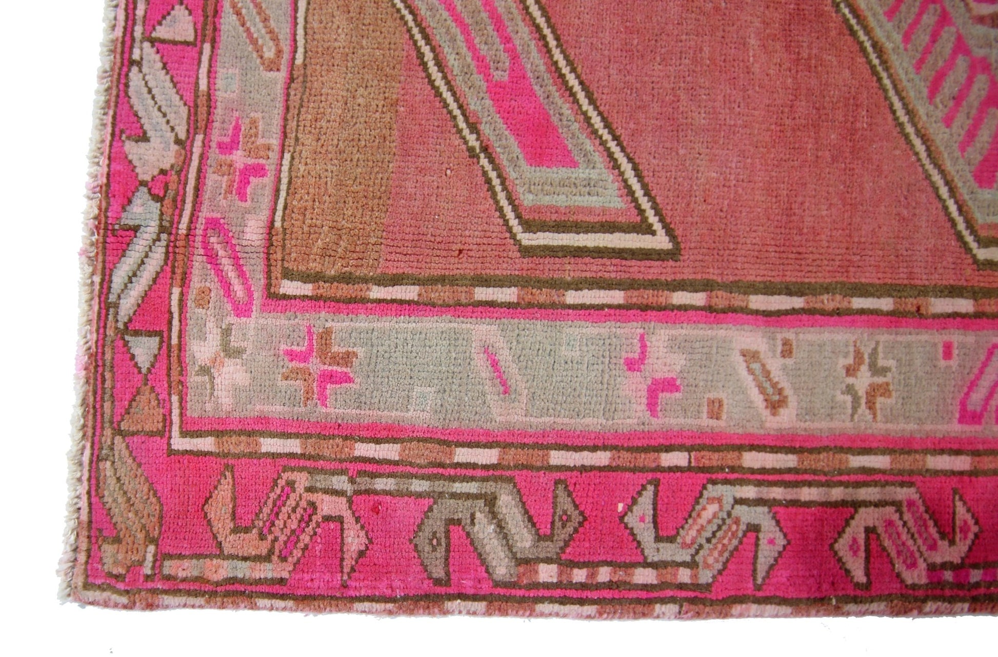 A close-up of a vintage Persian Ardabil rug featuring geometric patterns in pink and grey tones.