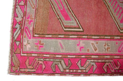 A close-up of a vintage Persian Ardabil rug featuring geometric patterns in pink and grey tones.