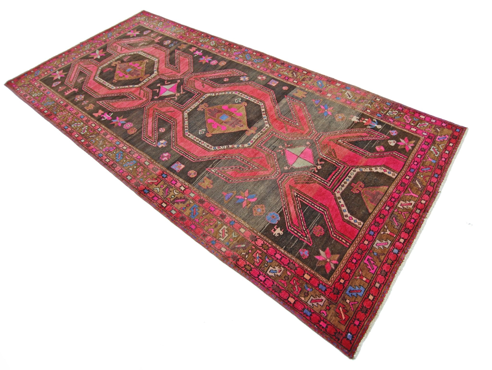 A vintage Persian Ardabil rug featuring geometric patterns in vibrant pink and brown tones.