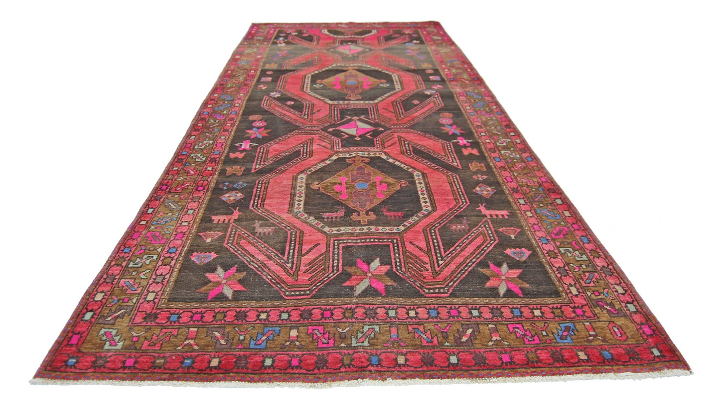 A vintage Persian Ardabil rug featuring a dark brown field with vibrant pink geometric patterns.