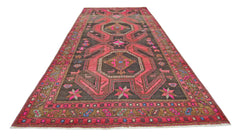 A vintage Persian Ardabil rug featuring a dark brown field with vibrant pink geometric patterns.
