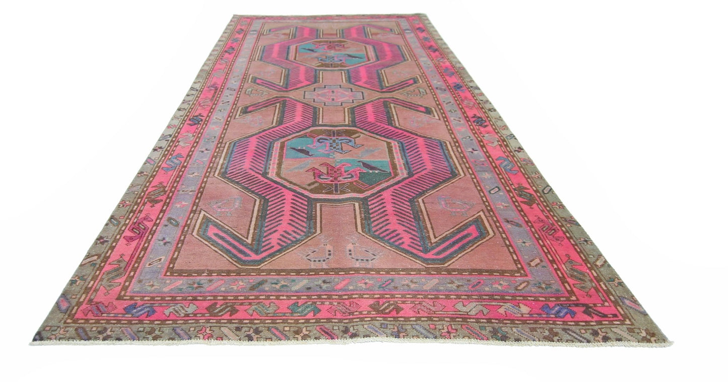 A vintage Persian Ardabil rug featuring a geometric pattern in vibrant pink and muted earth tones.
