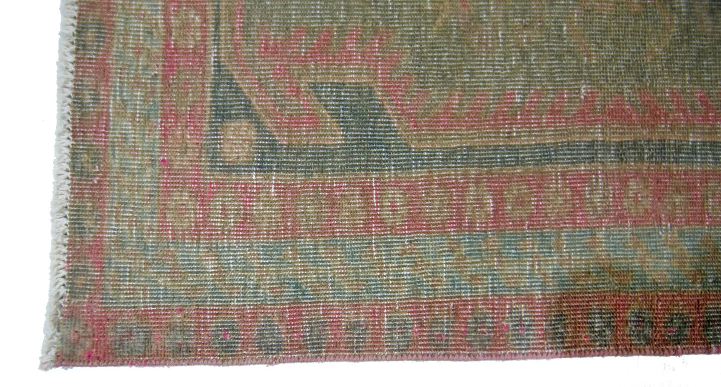 A close-up of a vintage Persian Ardabil rug featuring a faded geometric border in pink and green.