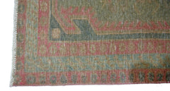 A close-up of a vintage Persian Ardabil rug featuring a faded geometric border in pink and green.