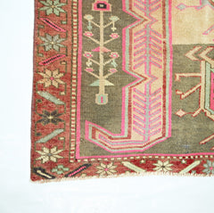 A corner view of a vintage Persian Ardabil runner featuring geometric floral motifs in pink and green.
