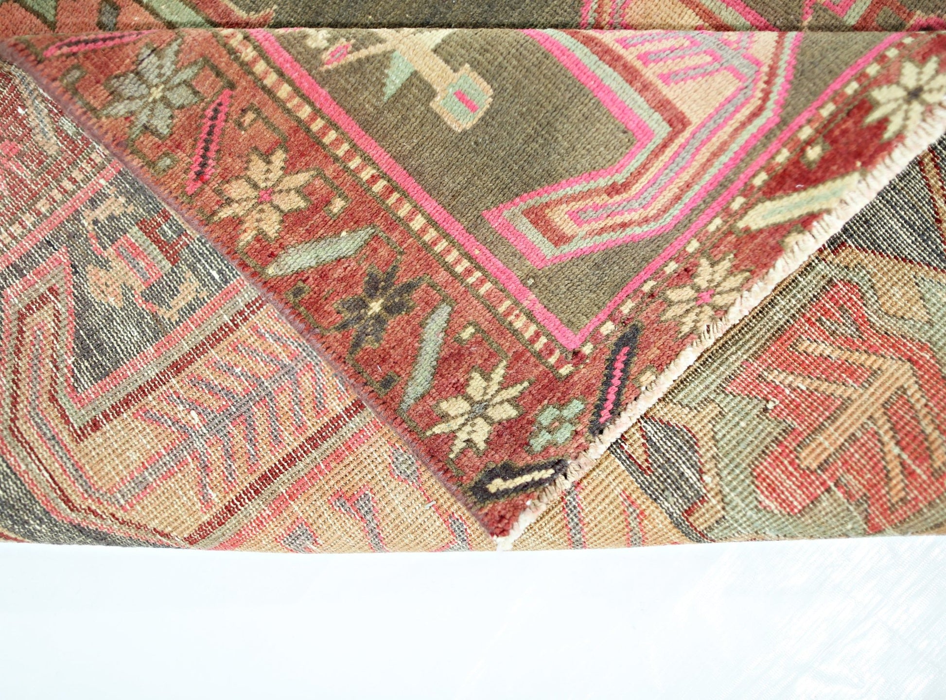 A folded vintage Persian Ardabil runner featuring intricate geometric patterns in red and green.