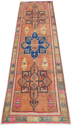 A vintage Persian runner featuring geometric medallions in blue and pink on an orange background.