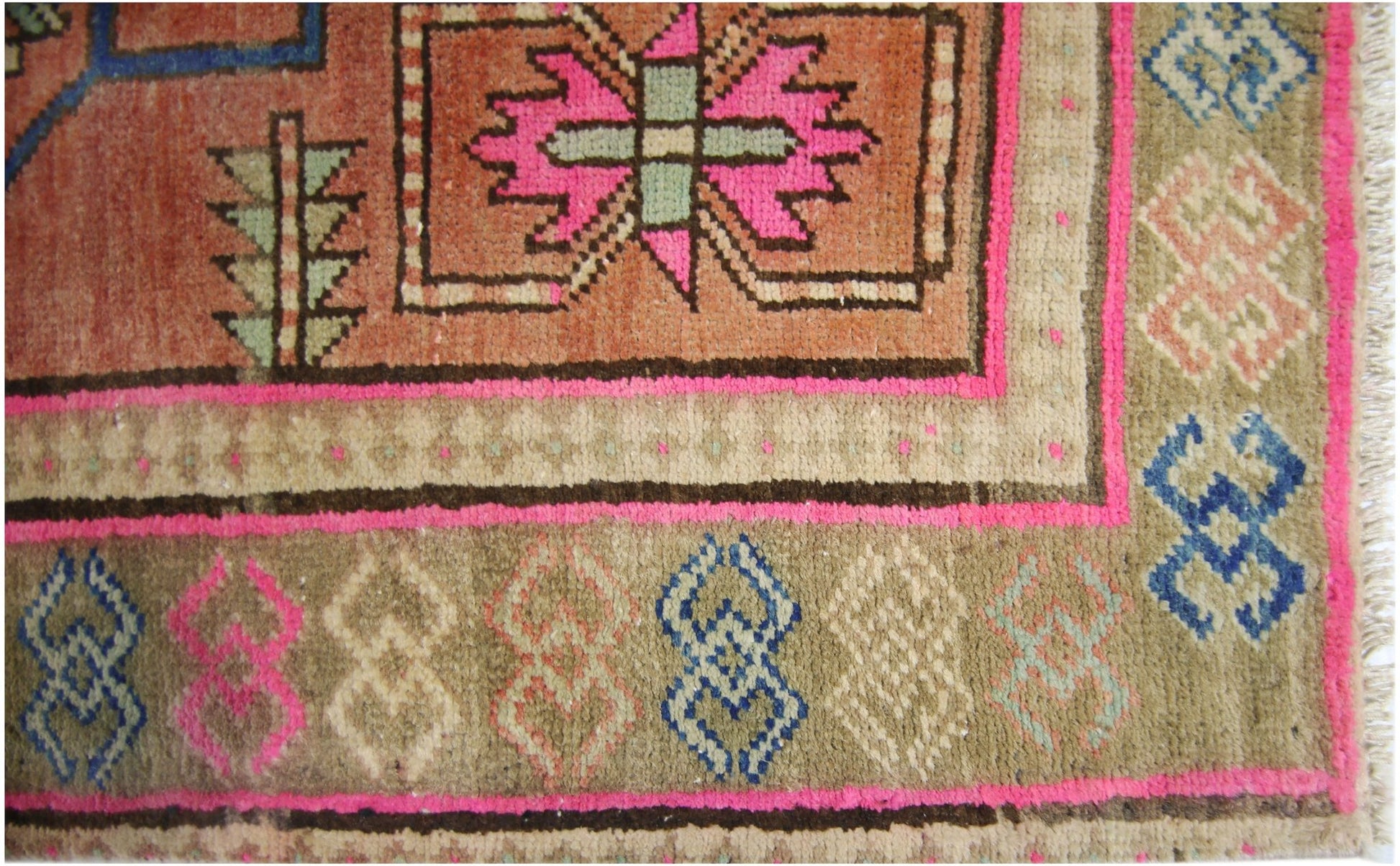 A vintage Persian runner featuring geometric patterns in pink, blue, and tan on a wool pile.