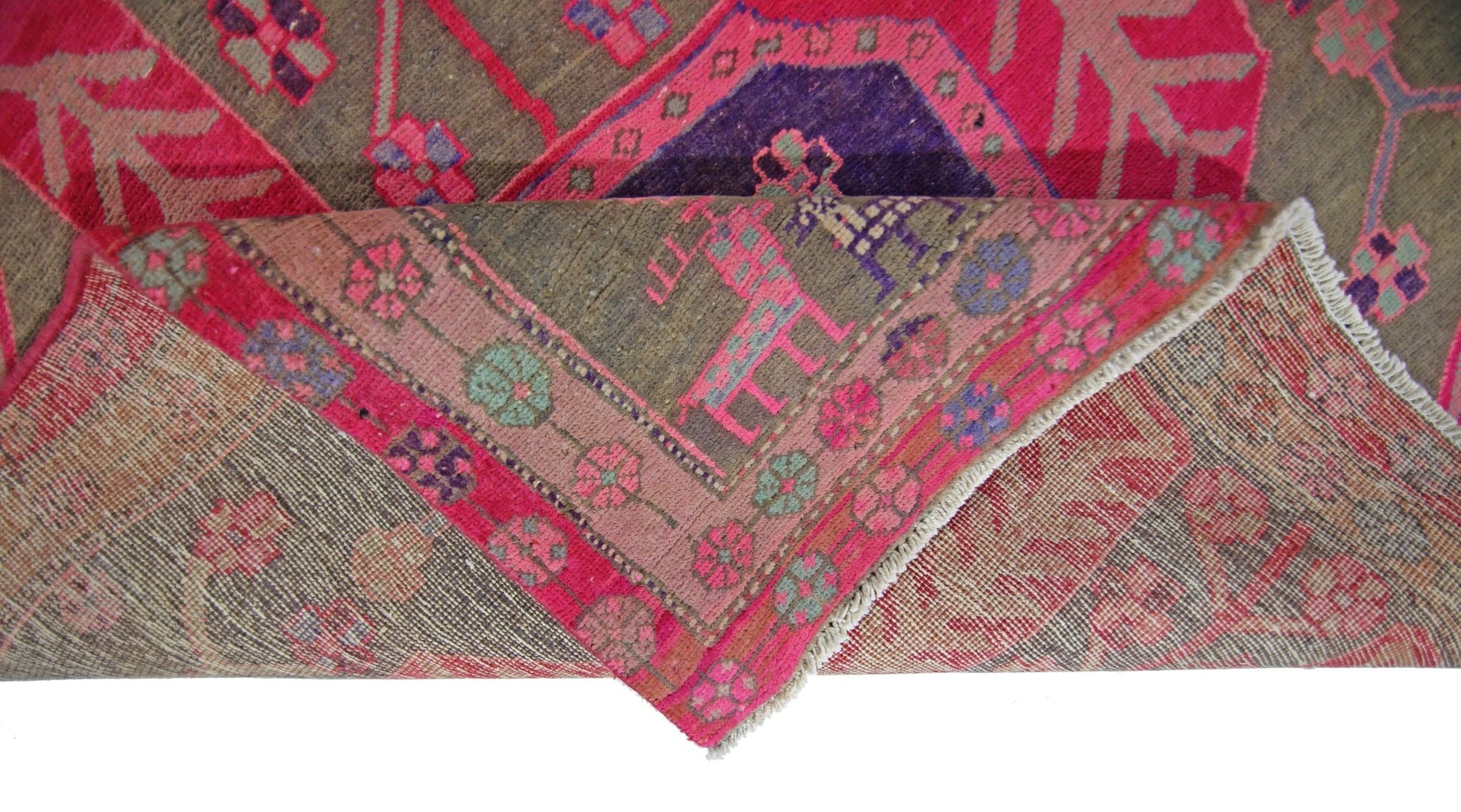 A vintage Persian Ardabil rug with a folded corner revealing its intricate floral pattern.