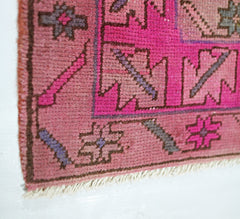 A close-up of a vintage Persian Ardabil runner featuring geometric patterns in pink and grey wool.