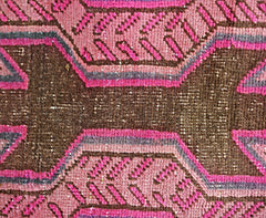 A close-up of a vintage Persian Ardabil runner featuring geometric patterns in pink and brown.