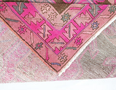 A corner view of a vintage Persian Ardabil runner featuring a vibrant pink and brown geometric pattern.