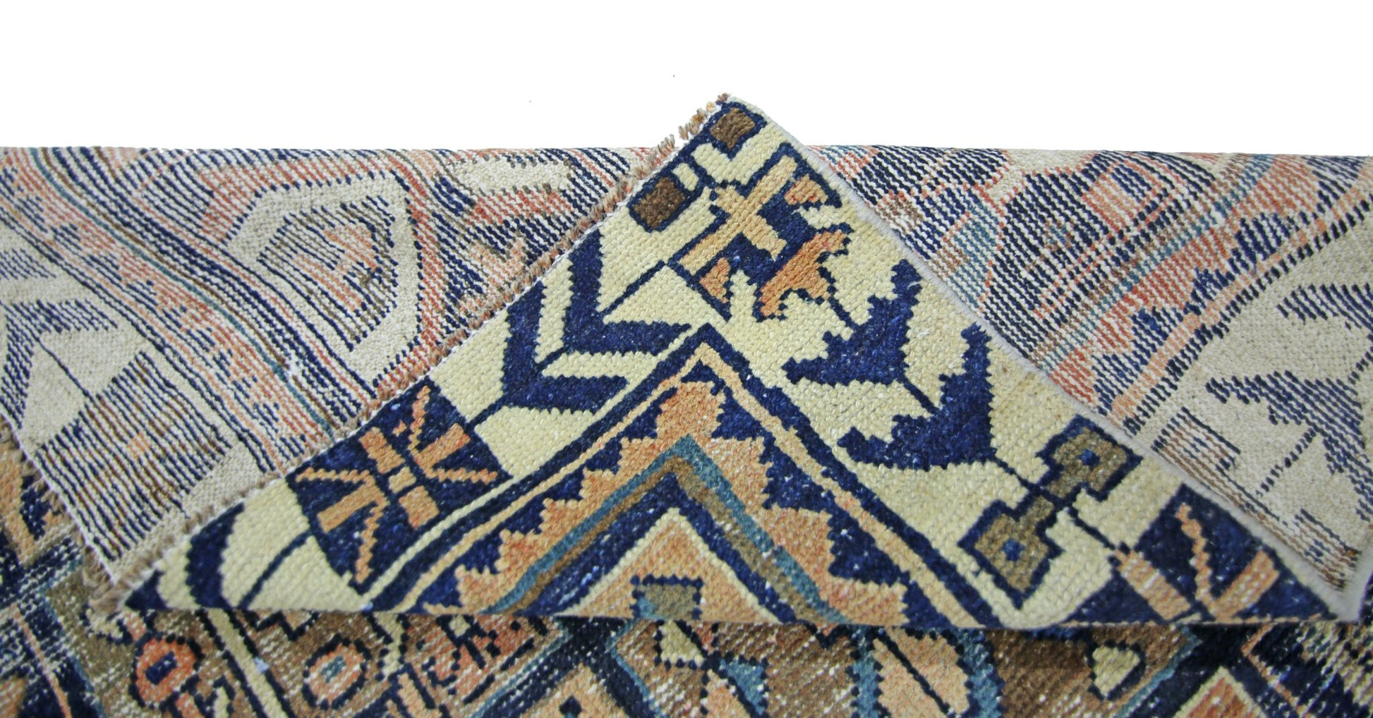A corner of a vintage Persian Bakhtiari rug is folded over to reveal its intricate blue and tan pattern.
