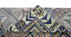 A corner of a vintage Persian Bakhtiari rug is folded over to reveal its intricate blue and tan pattern.