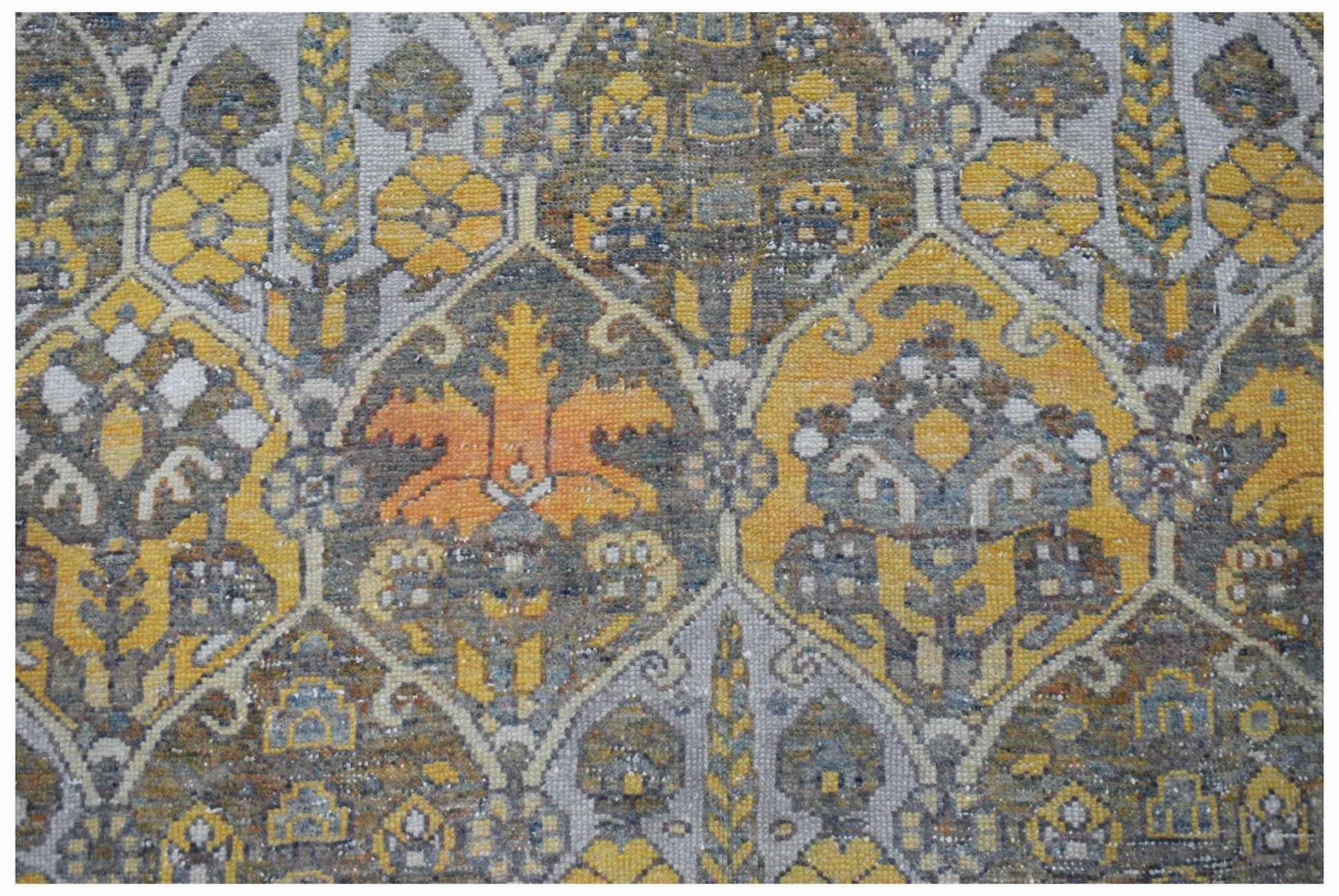 A vintage Persian Bakhtiari rug featuring a repeating geometric pattern in yellow, grey, and orange.