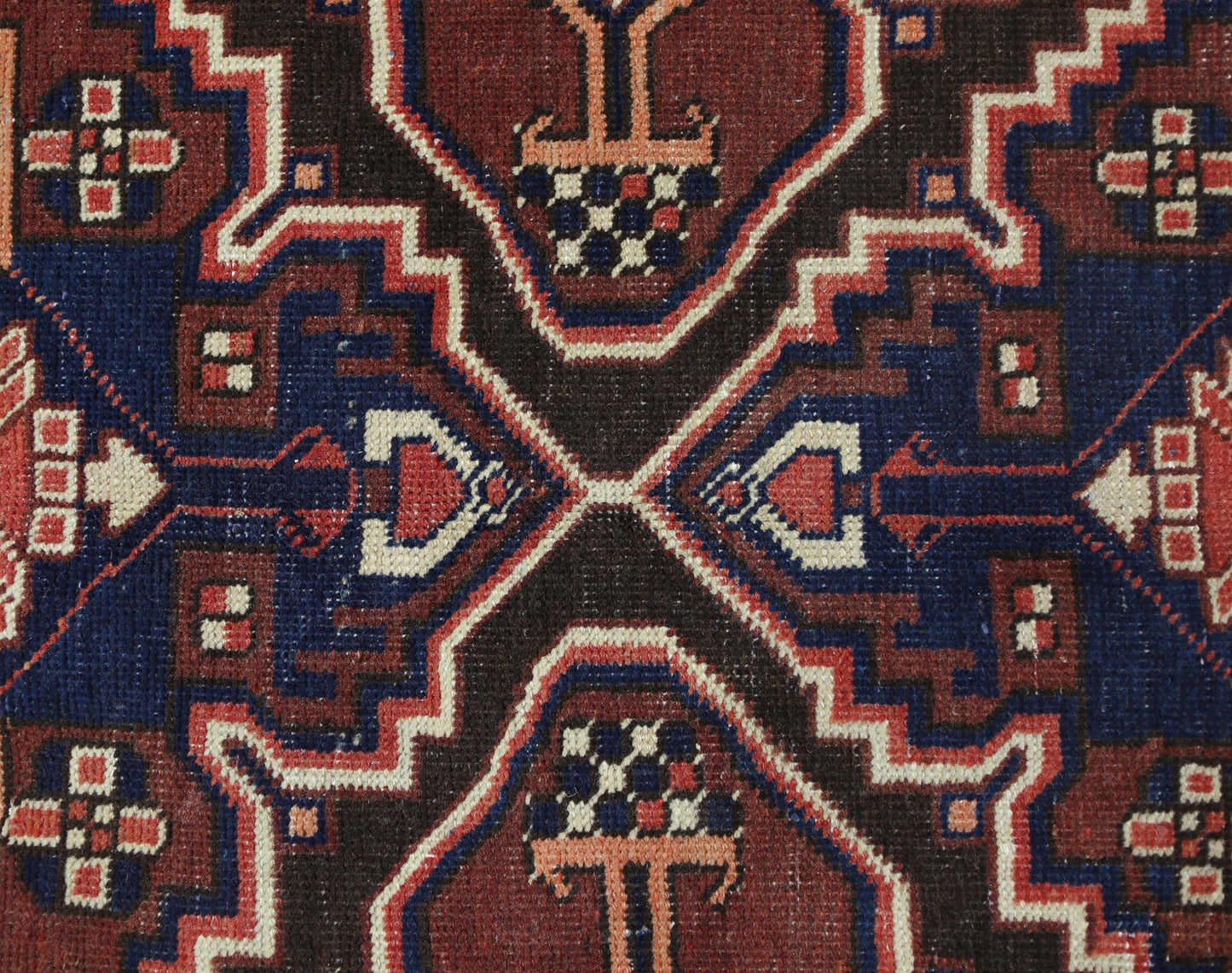 A close-up of a vintage Persian Bakhtiari rug featuring geometric floral motifs in red and blue.