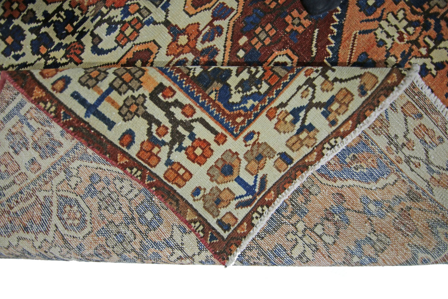 A corner of a vintage Persian Bakhtiari rug is folded back to show its intricate floral pattern.