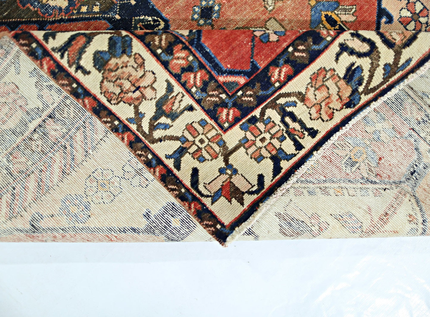 A vintage Persian Bakhtiari rug with a folded corner revealing its intricate floral pattern.