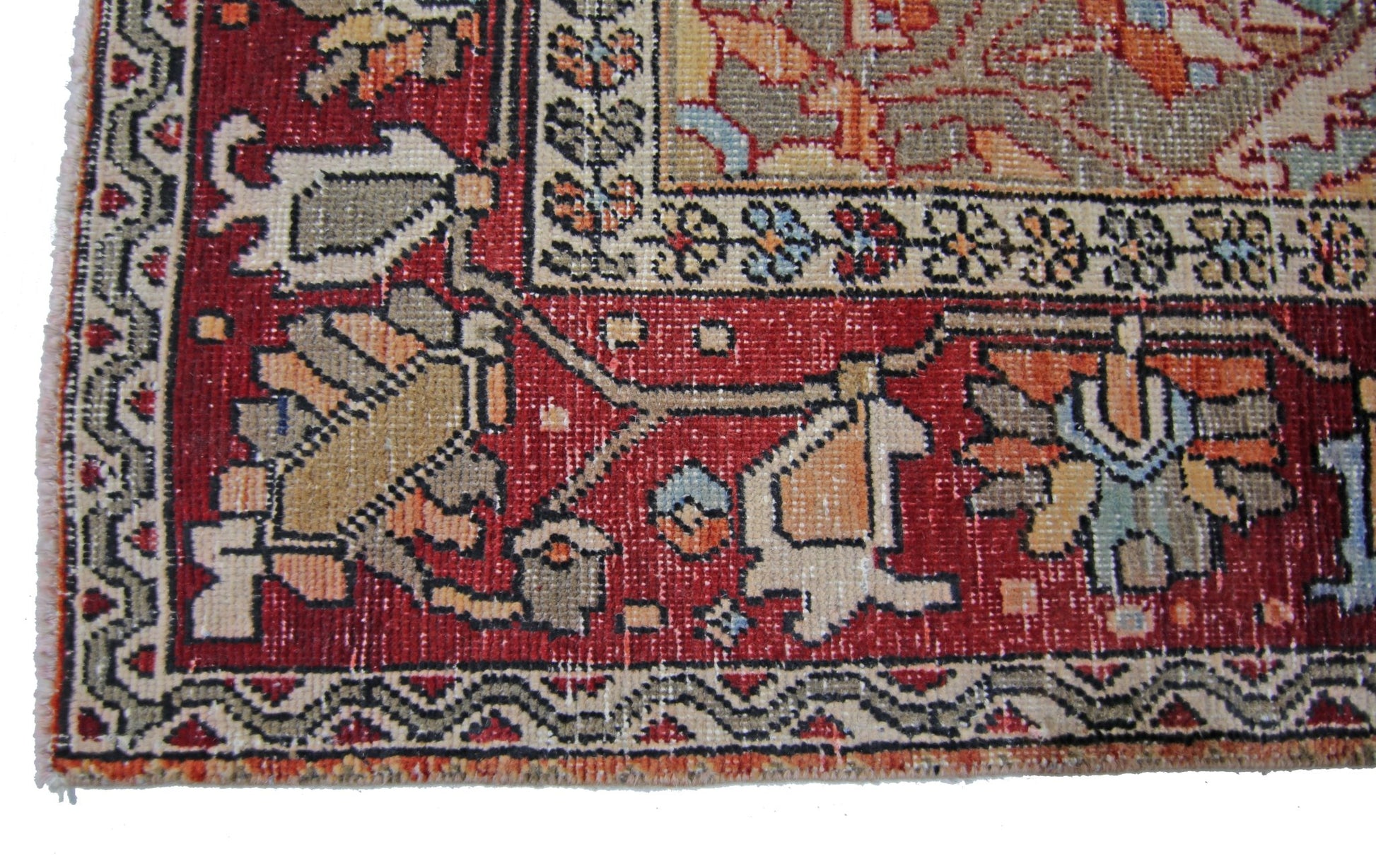 A corner view of a vintage Persian Tabriz rug featuring intricate floral patterns in red and beige.
