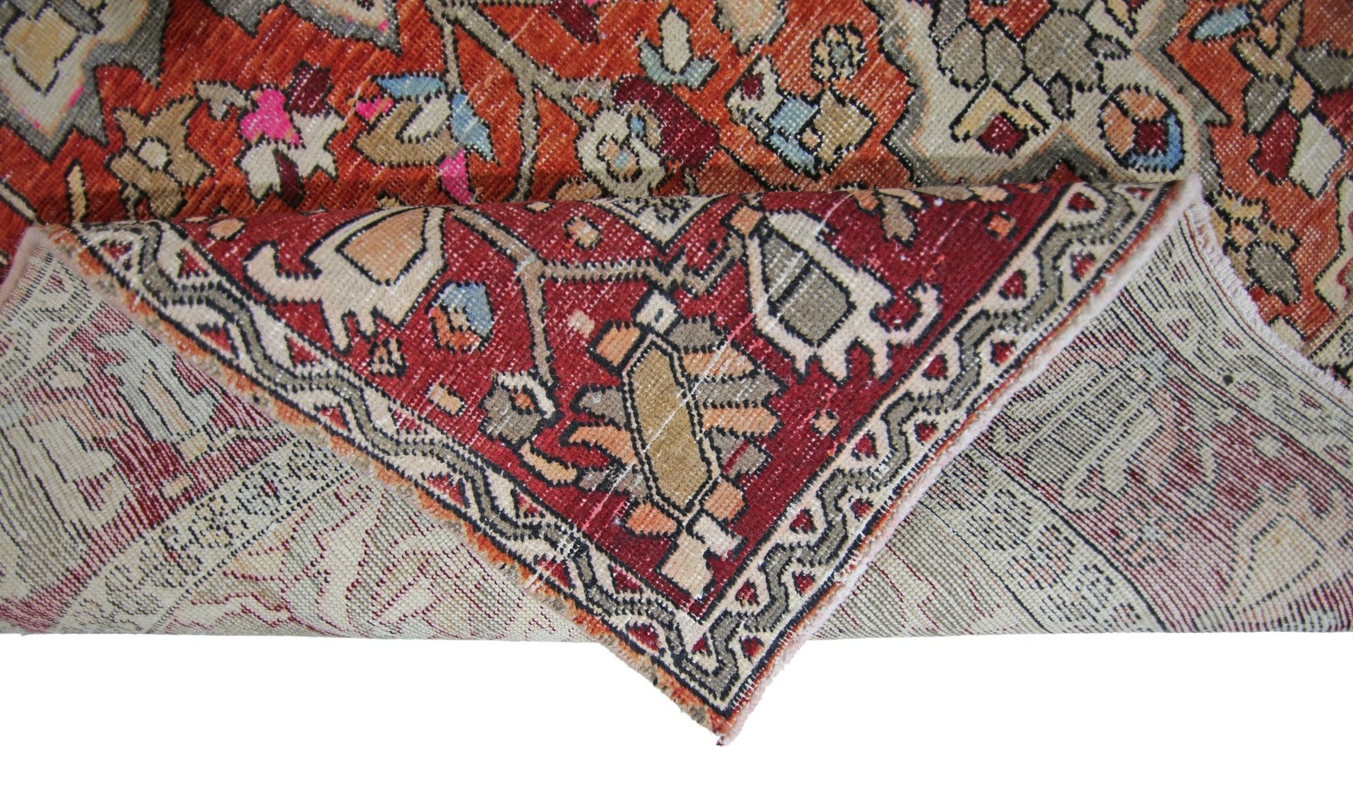 A corner of a vintage Persian Tabriz rug is folded back to reveal its intricate red and orange pattern.