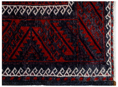 A close-up of a vintage Afghan Baluch rug featuring geometric patterns in red and dark blue.