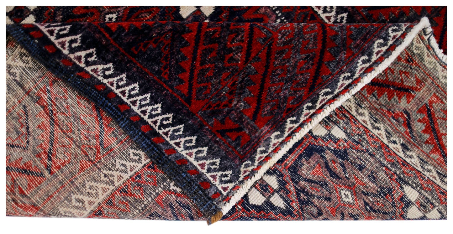 A corner of a vintage Afghan Baluch rug is folded back to reveal its intricate red and blue pattern.