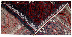 A corner of a vintage Afghan Baluch rug is folded back to reveal its intricate red and blue pattern.