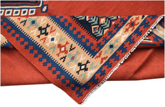 A folded vintage Persian kilim rug featuring geometric patterns in red, blue, and beige wool.