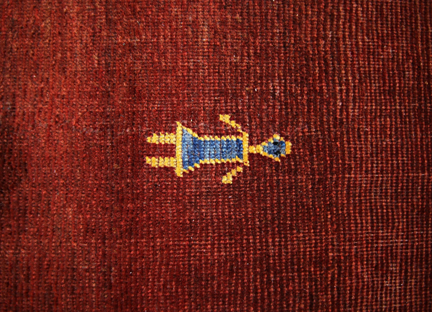 A close-up of a vintage Persian Shiraz rug featuring a small, stylized blue and yellow figure on a deep red wool background.