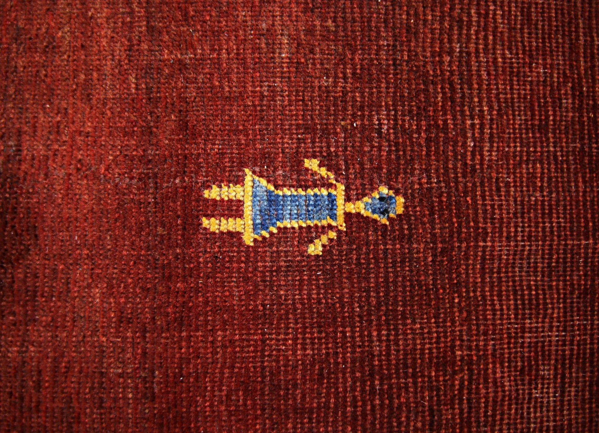 A close-up of a vintage Persian Shiraz rug featuring a small, stylized blue and yellow figure on a deep red wool background.