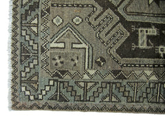 A vintage Persian rug featuring geometric patterns in shades of grey and brown.