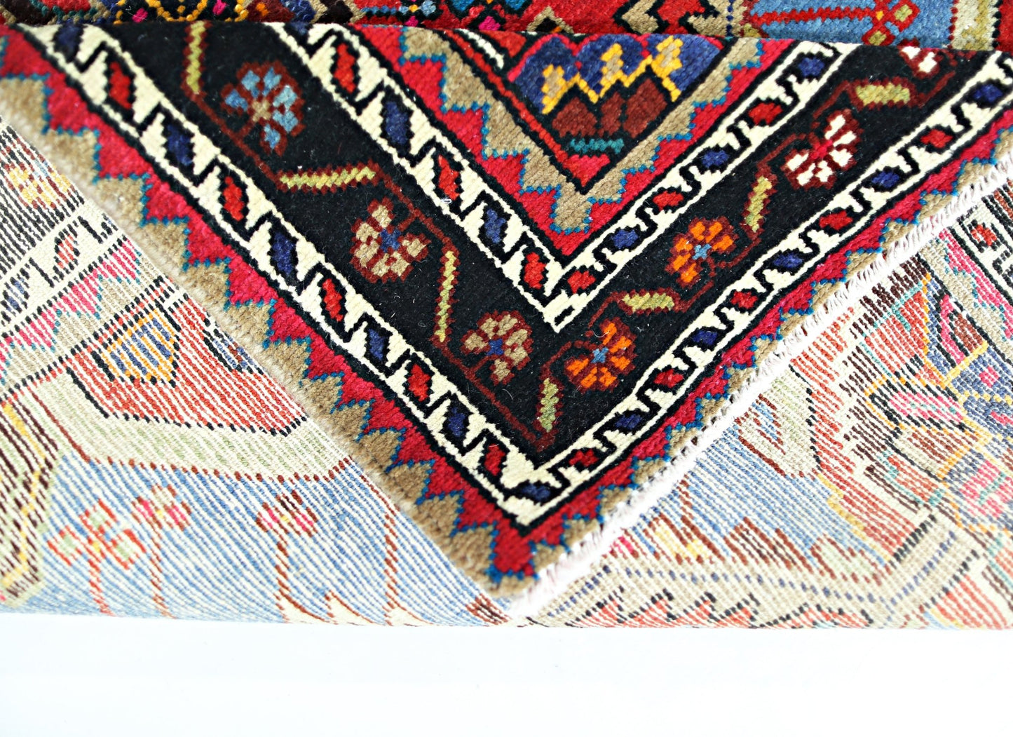 A folded vintage Persian Hamadan rug featuring intricate geometric patterns in red, blue, and black.