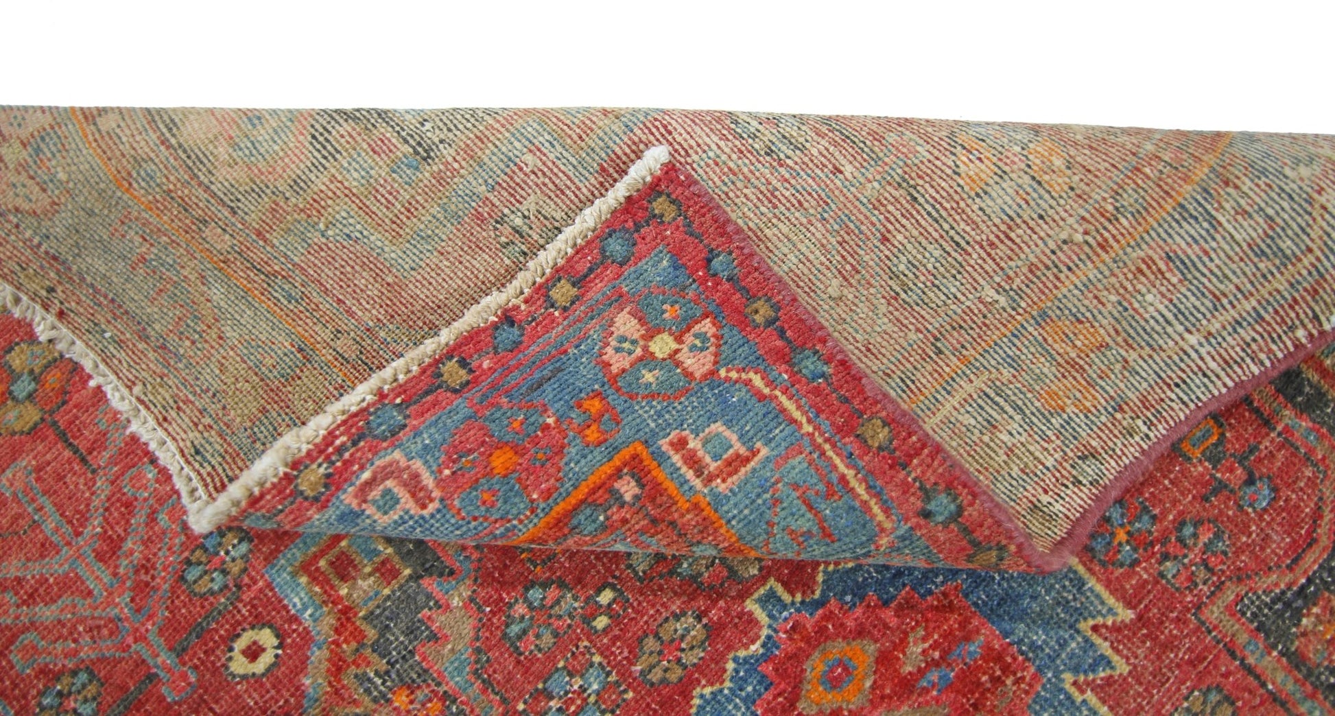 A corner of a vintage Persian Hamadan rug is folded back to reveal its wool pile and cotton base.