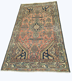 A vintage handmade Persian rug featuring a geometric medallion pattern in muted red and blue tones.