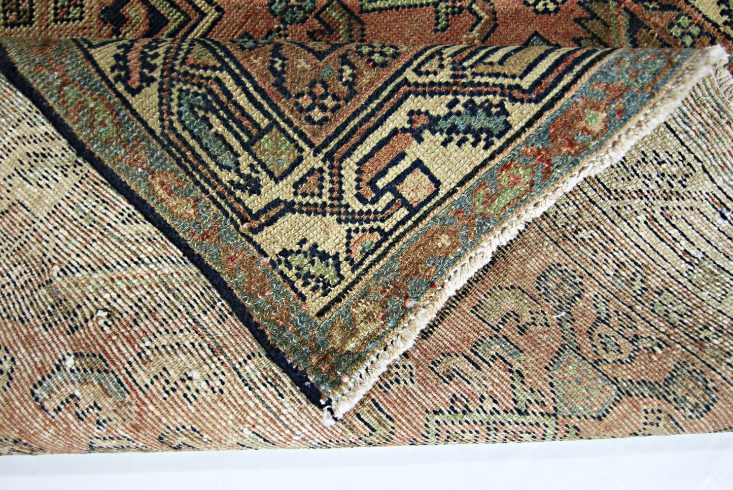 A folded vintage Persian rug featuring intricate geometric patterns in muted earth tones.