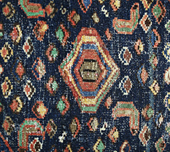 A close-up of a vintage Persian Hamadan rug featuring a geometric medallion on a dark blue field.